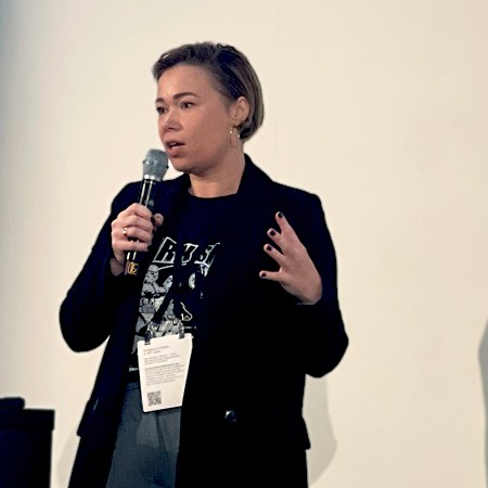 Katerina Timofejeva speaking on stage with a microphone